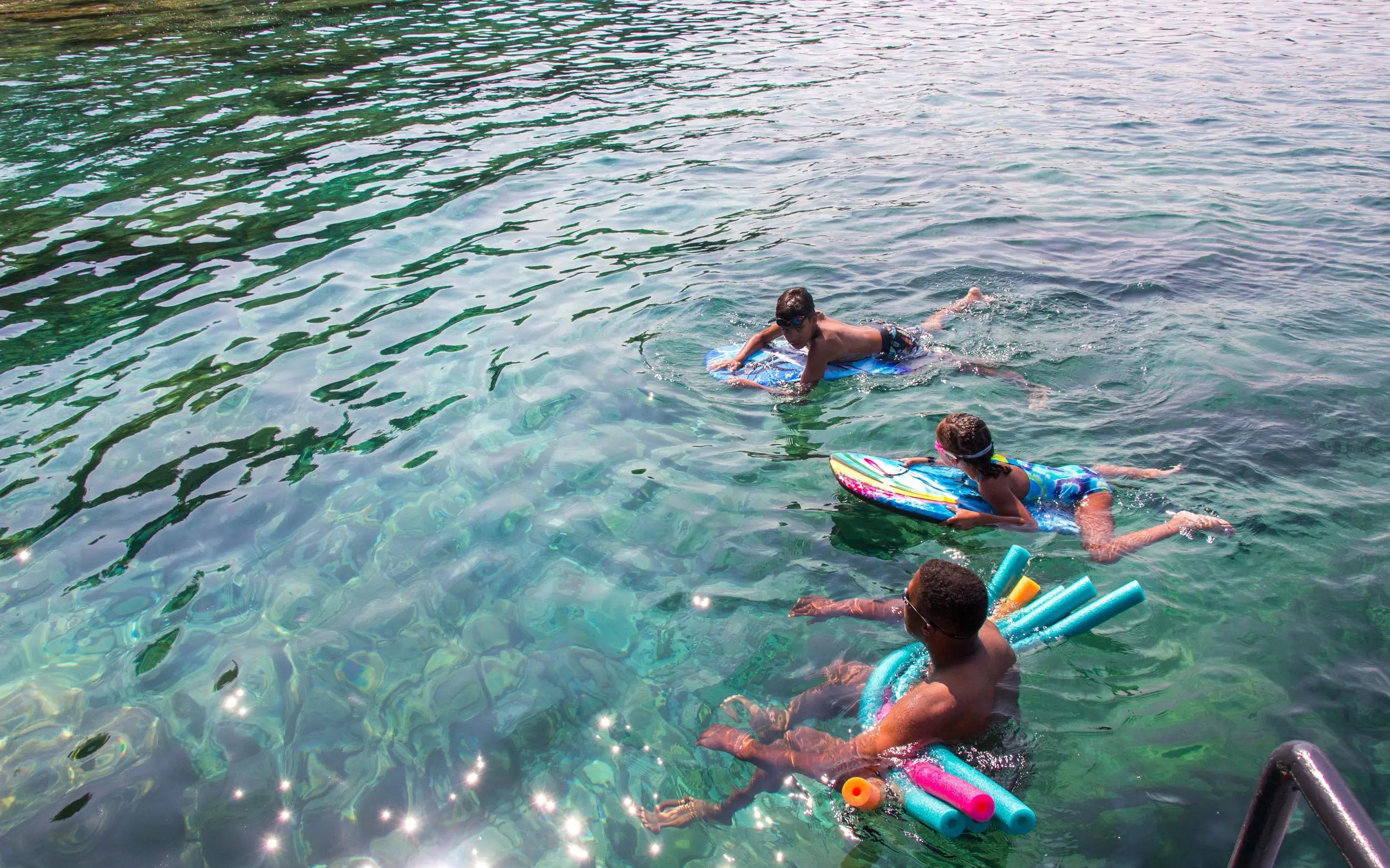 A dad with his son and daughter swimming in crystal-clear water.