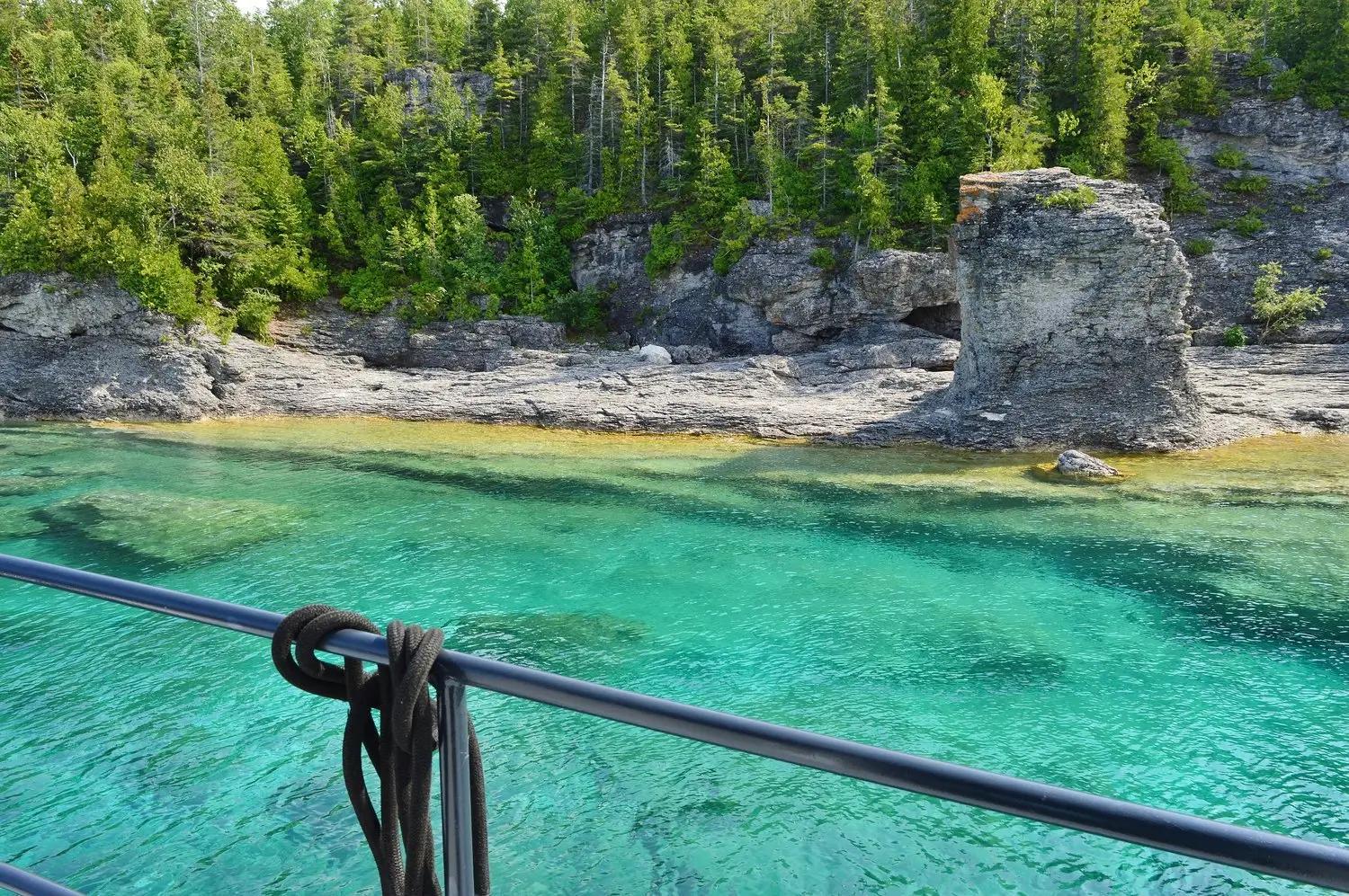 A rocky shoreline featuring a rock formation known as a Flowerpot, coniferous trees, and crystal-clear blue water.