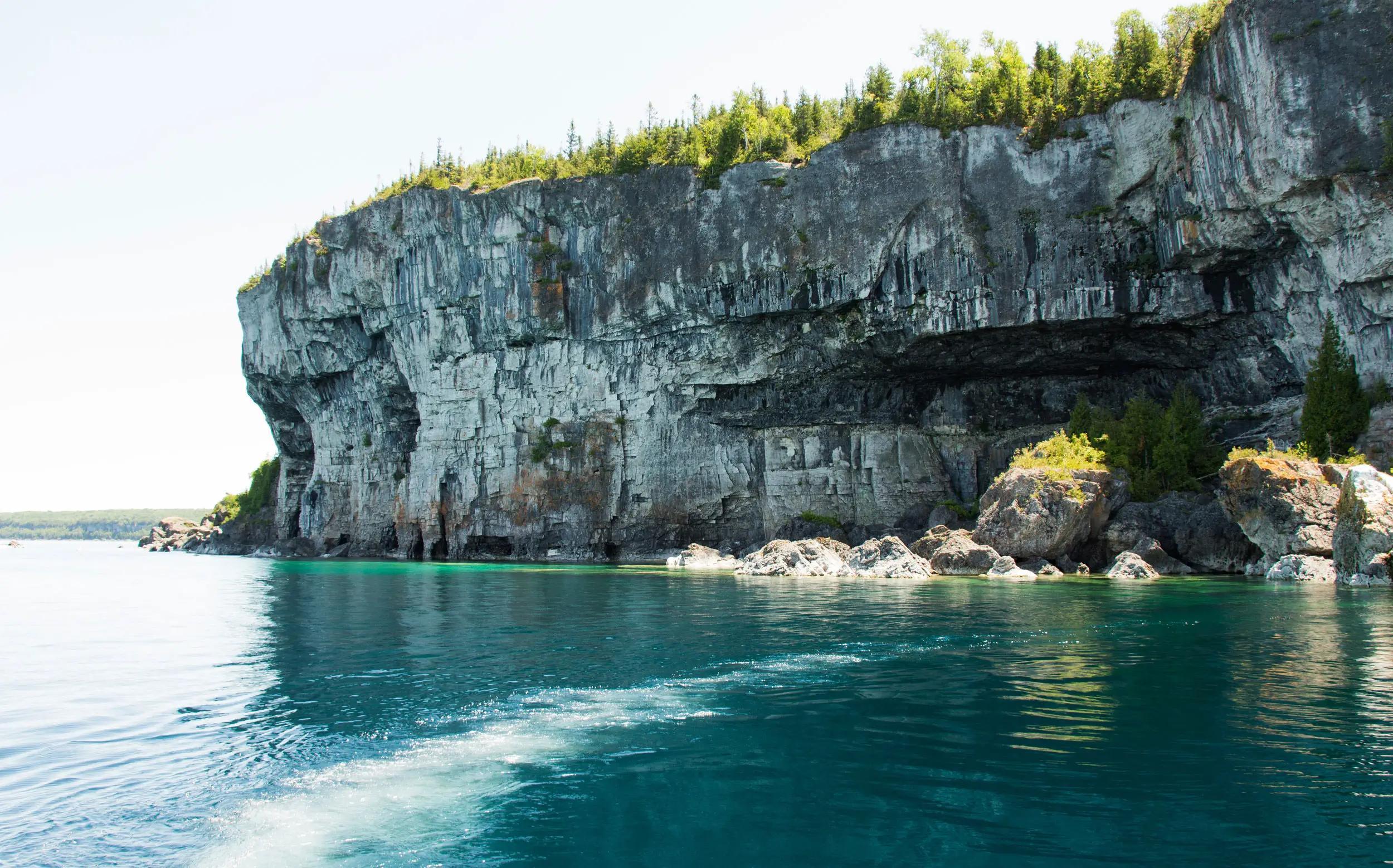 A large rocky cliff overlooking clear, blue water.